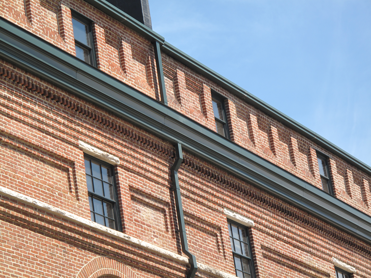 alt="Historic brick building finished with new metal roofing and siding in forest green"