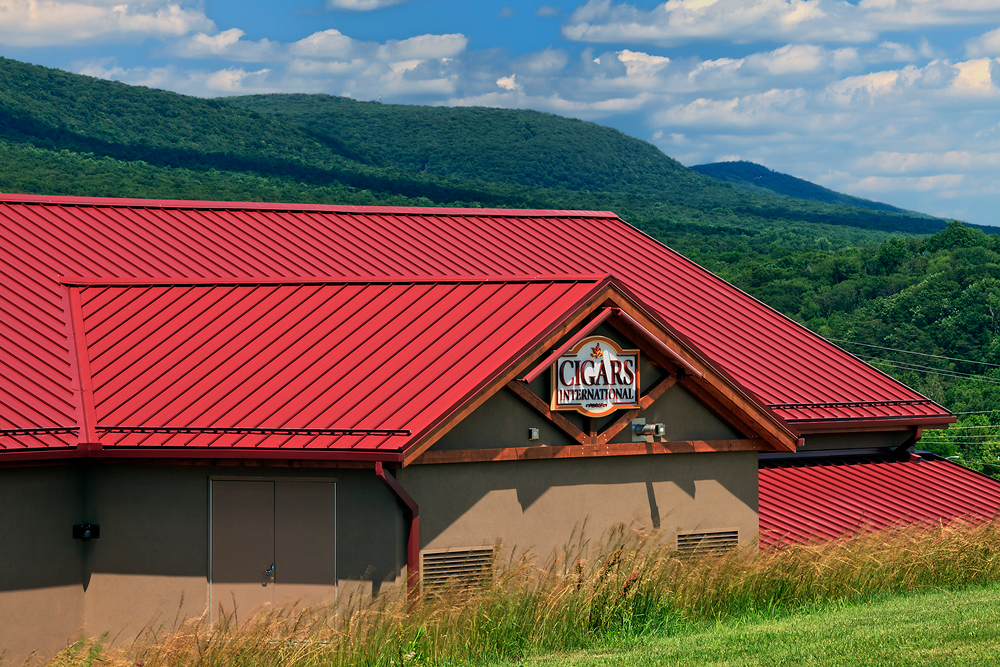 A view of a Cigars International building with a bright red metal roof in the mountains.