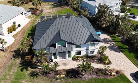 A charcoal metal roof on a white home surrounded by palm trees.